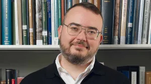 Man in a black cardigan in front of a bookshelf